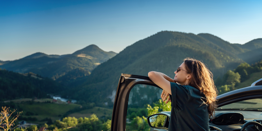 Frau lehnt in Autotür und geniesst Ausblick auf Berge